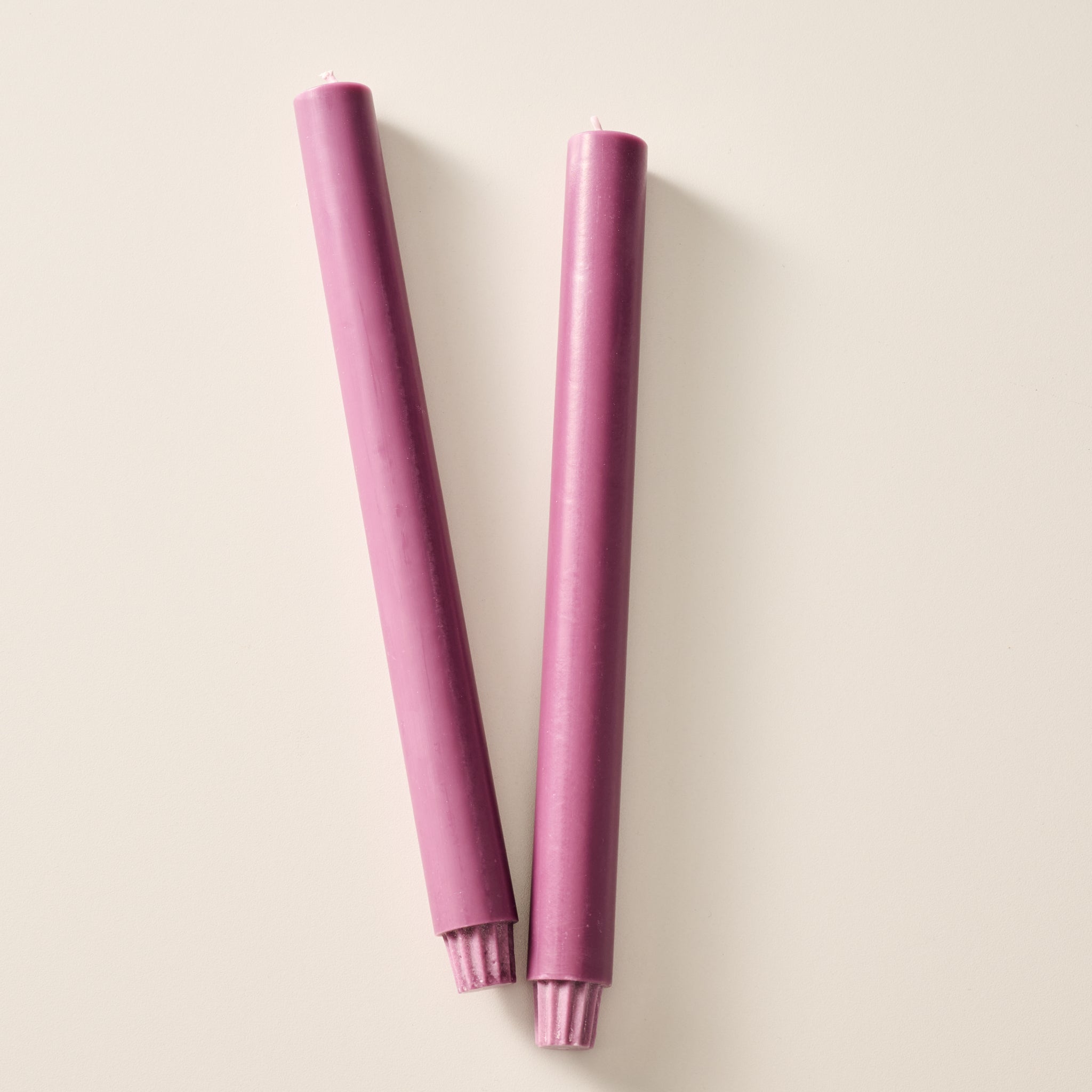 Two long, blackberry colored pillar candles laying flat on a light beige background.