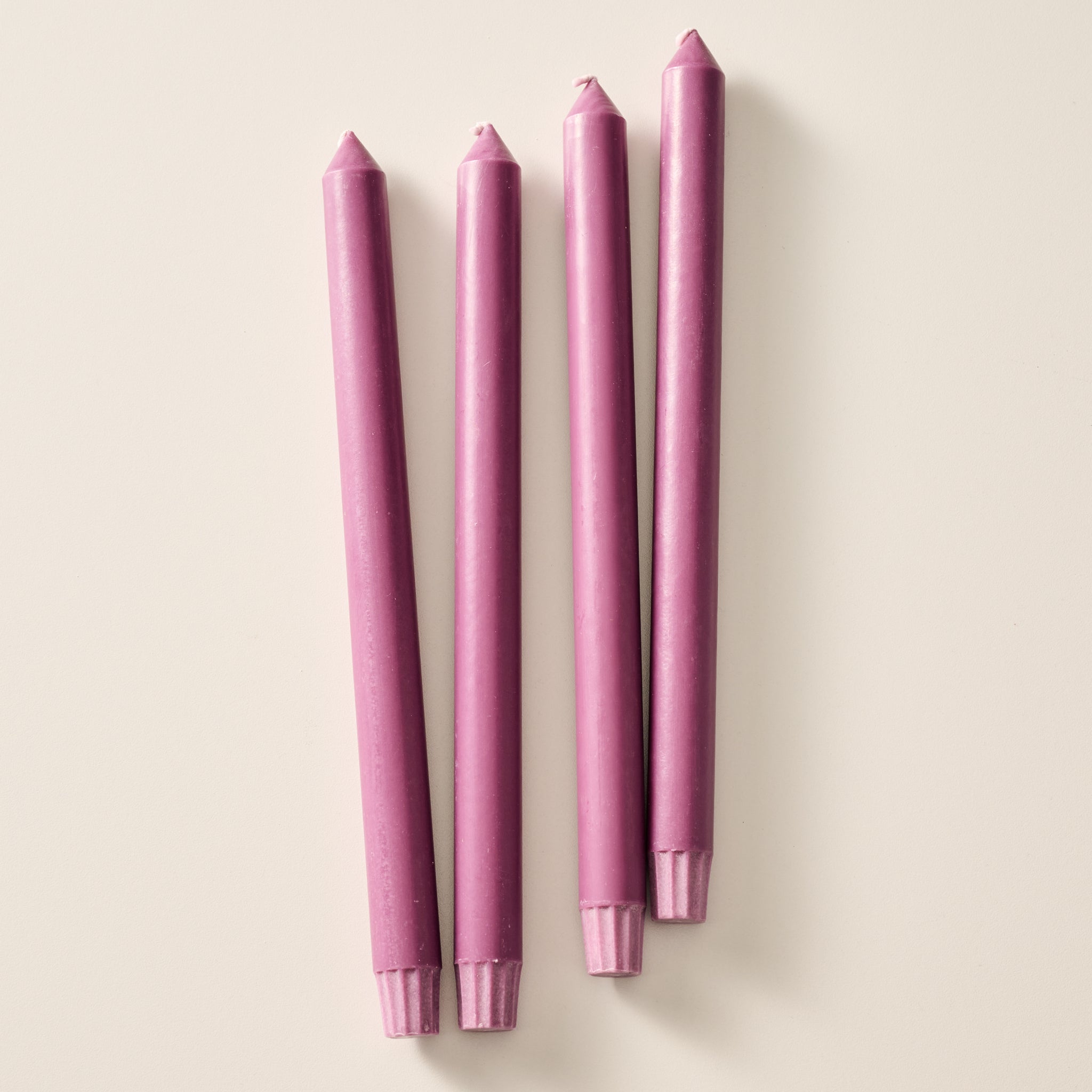 Four taper candles in a matching blackberry color, laying flat on a light beige background.