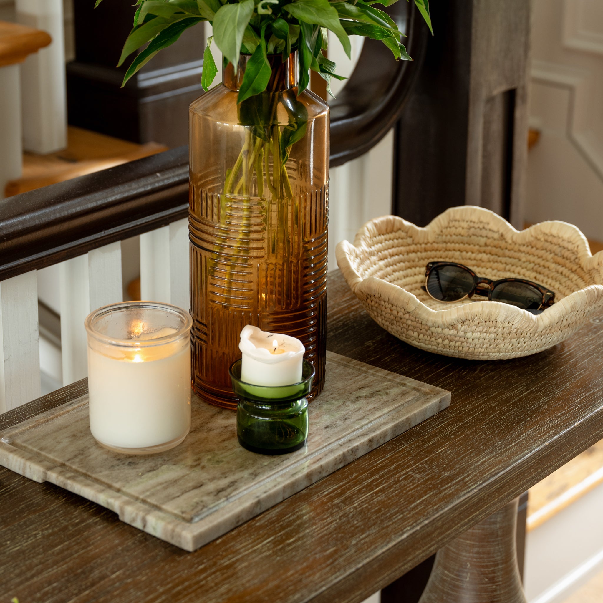 Decorative setting with candles, a vase, a bowl, and a marble board on a wooden surface.