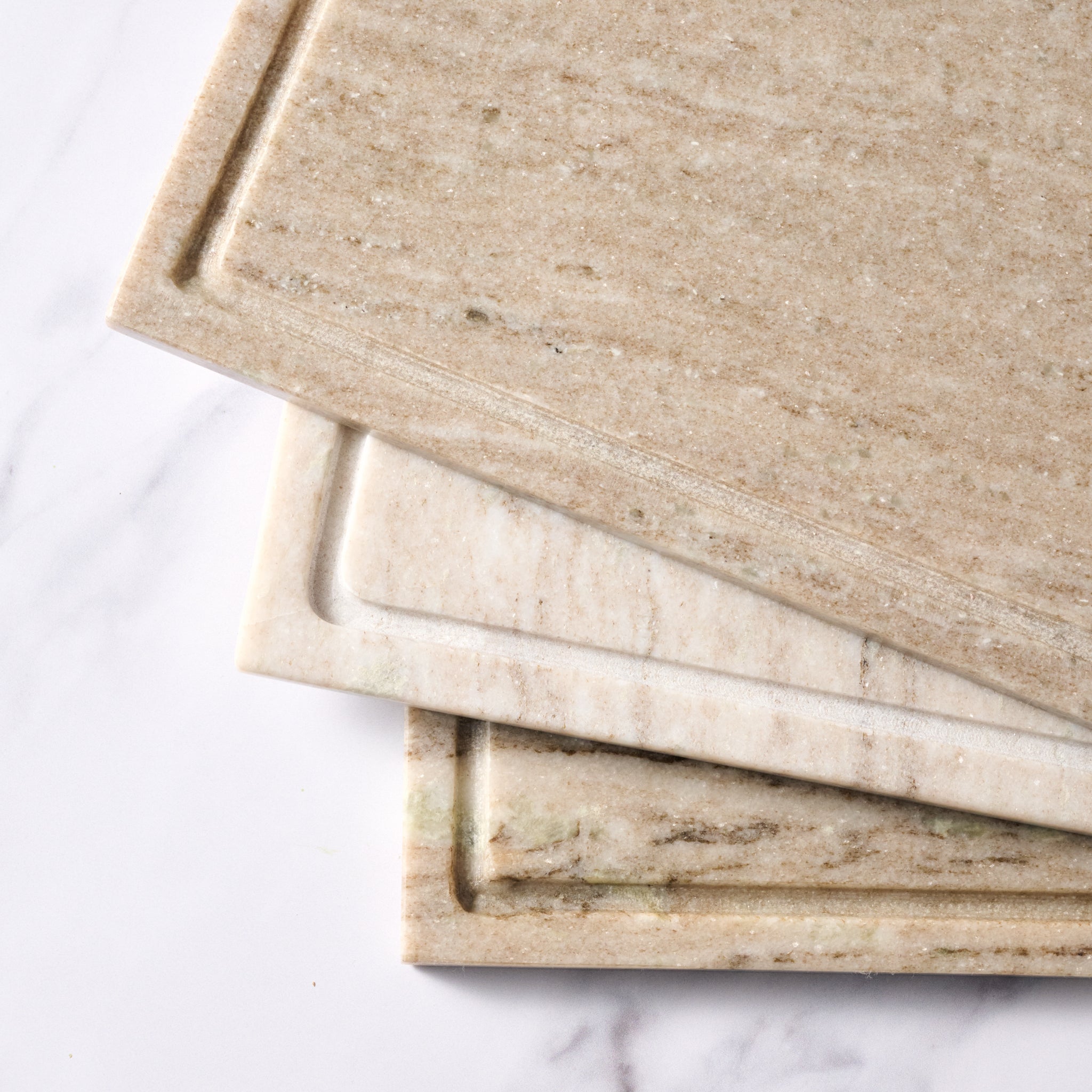 Three beige marble cutting boards stacked on a white marble surface