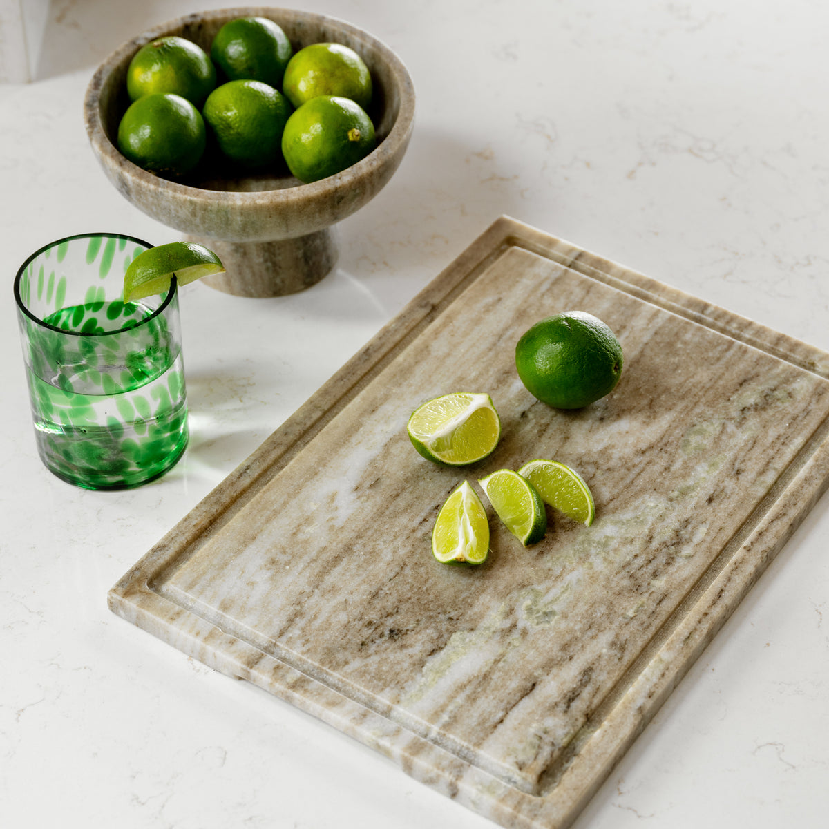 Limes on a marble cutting board with a glass of water on a white surface