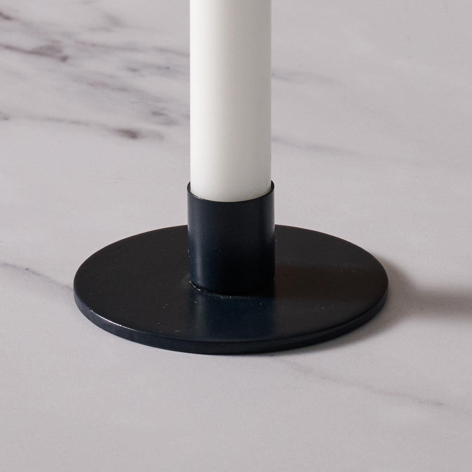 A close-up of a blue round candle holder base with a white candle inserted, set on a light marble surface.